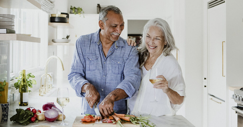 Senior couple prepping food in the kitchen, laughing and drinking wine.