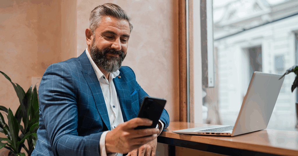 Main looking on smartphone while working at laptop