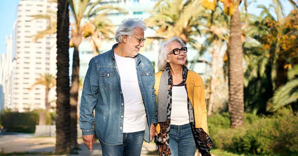 Retired American expat couple walking together through a sunny palm-lined city street