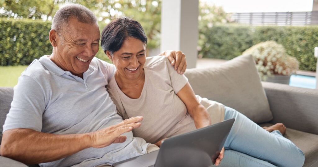 Older U.S. expat couple relaxing on an outdoor sofa, looking at a laptop together as they review their finances and plan for common financial obstacles while living abroad