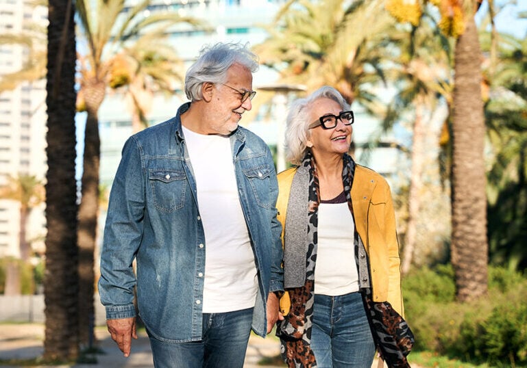 Older couple walking with palm trees in the background