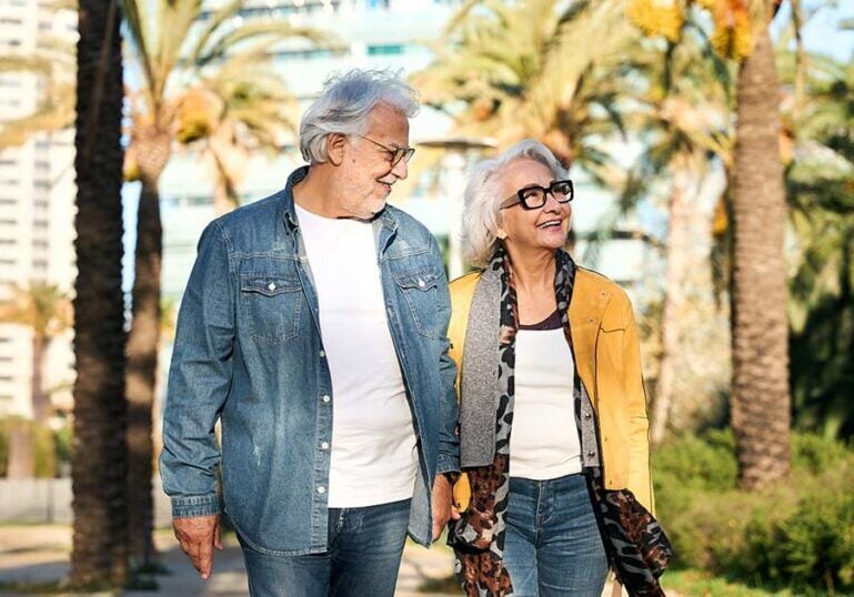 Retired American expat couple walking together through a sunny palm-lined city street