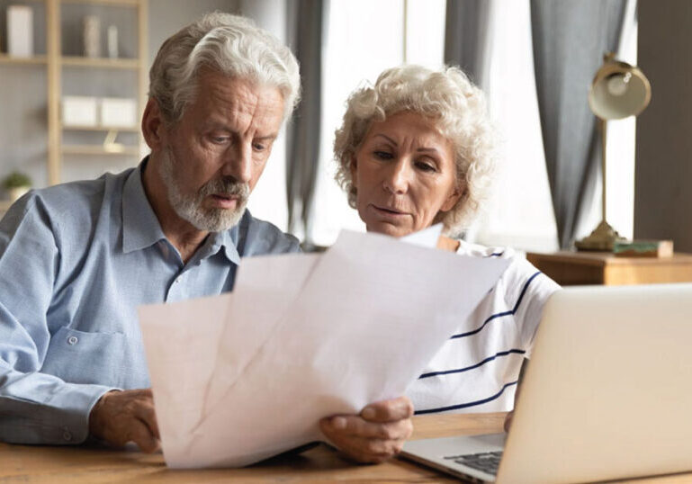 Retired couple looking at documents with a laptop.