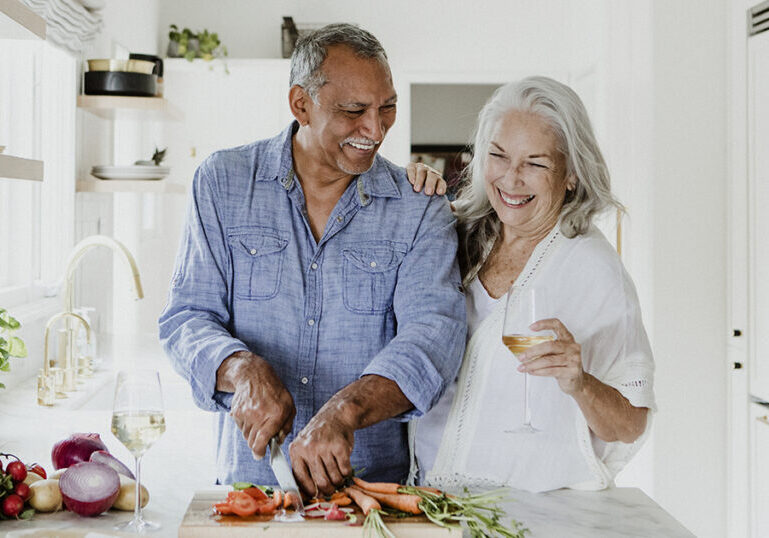 Senior couple prepping food in the kitchen, laughing and drinking wine.