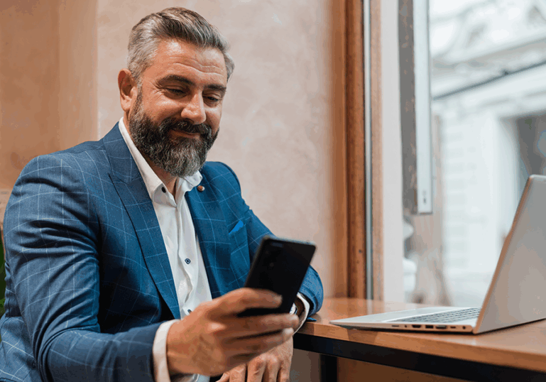 Main looking on smartphone while working at laptop