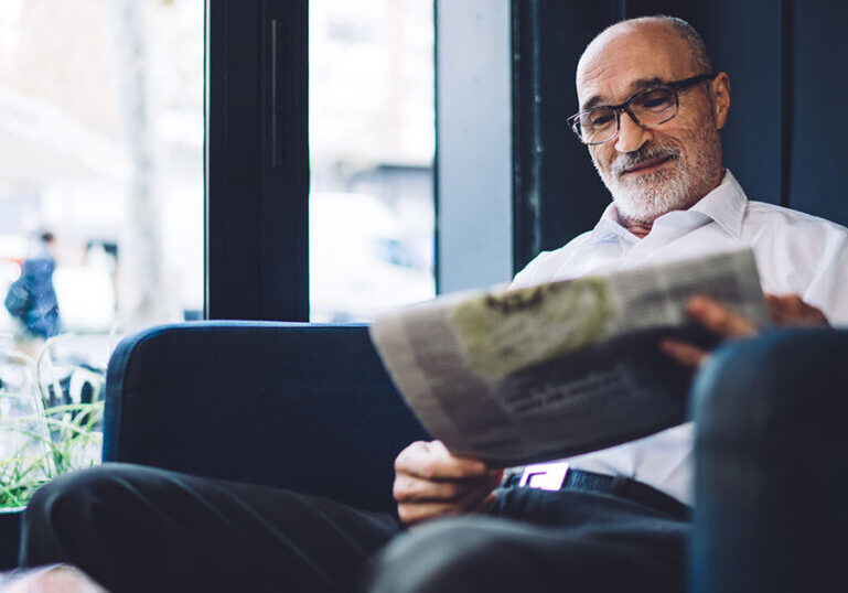 Retired American expat relaxing in a café abroad while reading a newspaper