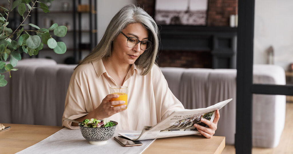 Middle-aged woman reading newspaper over breakfast while thinking about economic and political uncertainty