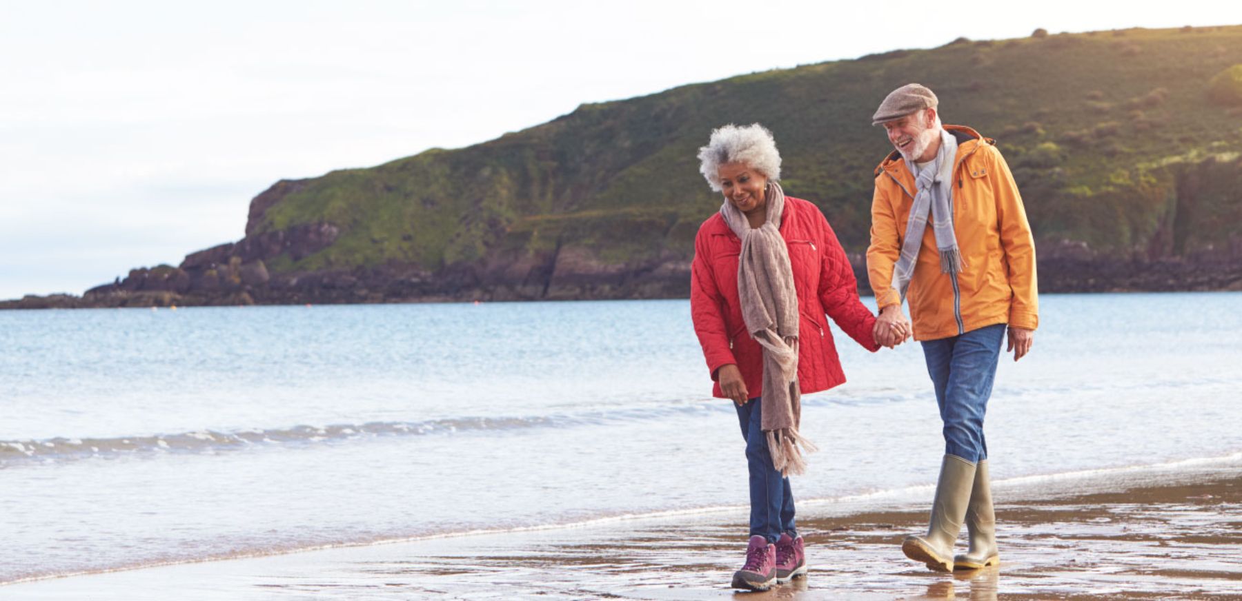 Senior couple holding hands and walking along shoreline.