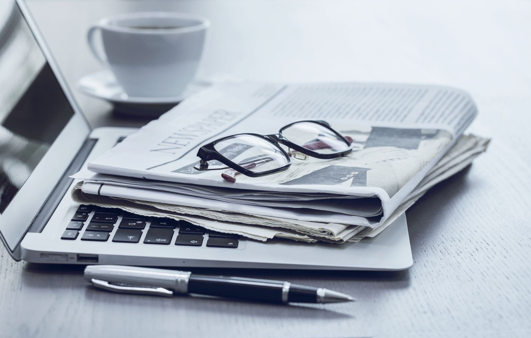 Newspaper with reading glasses sitting on top of laptop