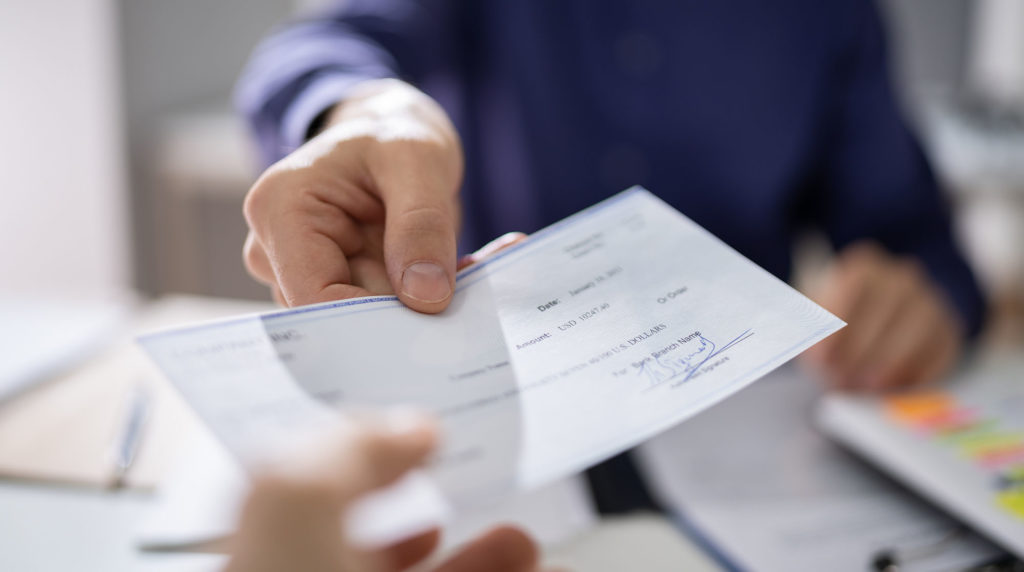 Man's hand passing along check to charity