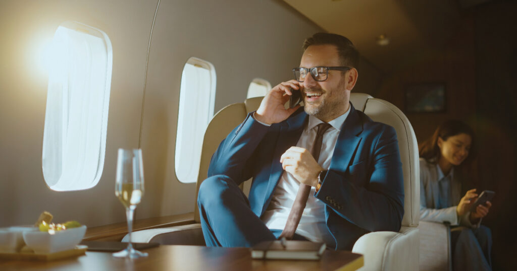 Businessman in a private jet talking on the phone with a glass of champagne on the table.