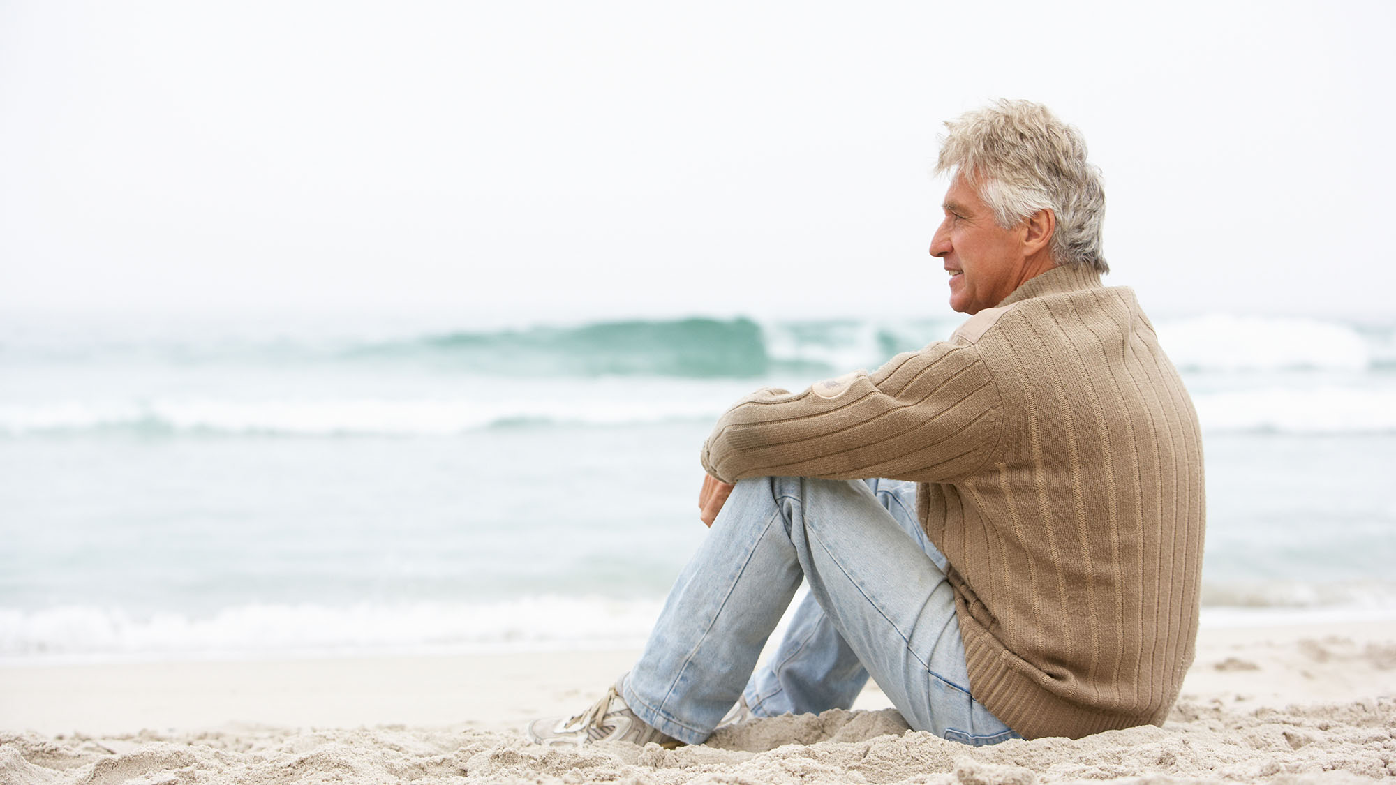 Man sitting on a beach viewing the calm waters