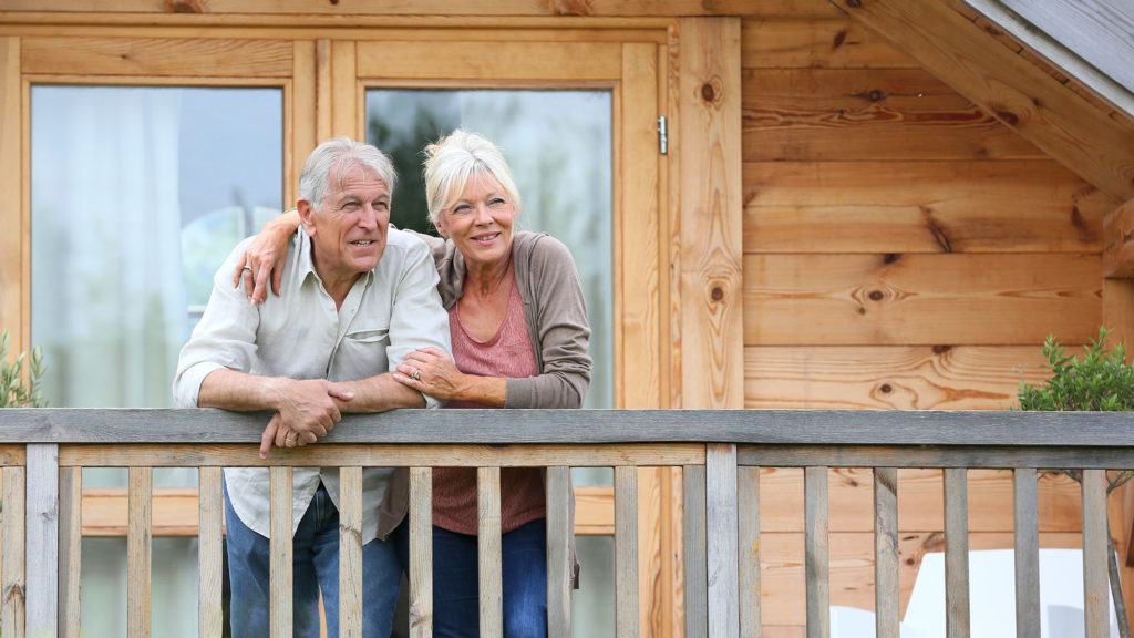 Senior couple standing oustide log cabin in countryside