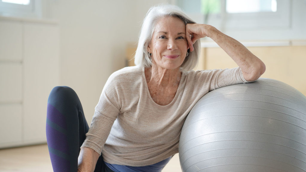 Smiling senior woman resting on a swiss ball at home