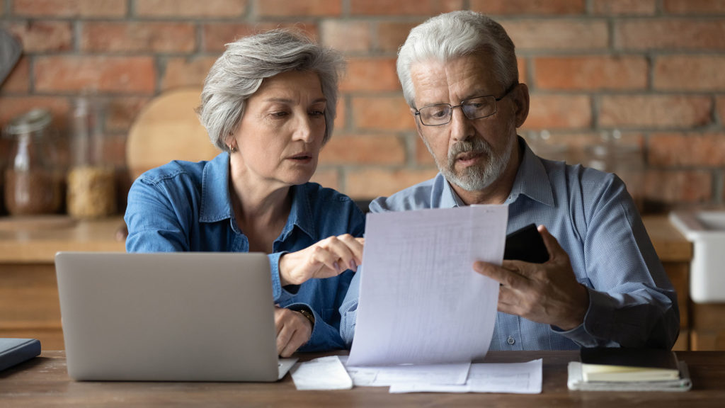 Mature couple compares notes between paperwork and laptop