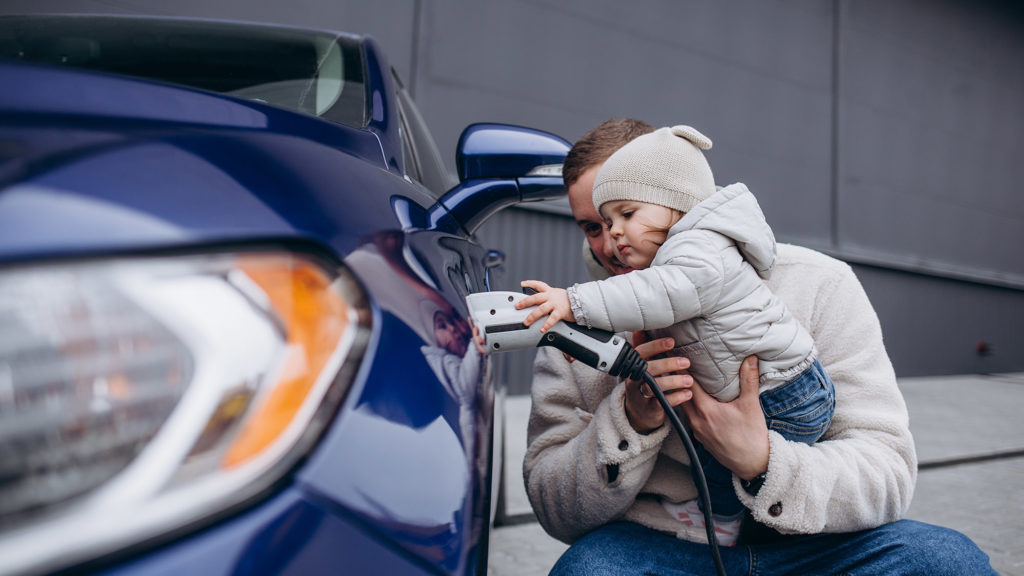 father playing with young daughter while charging electric car