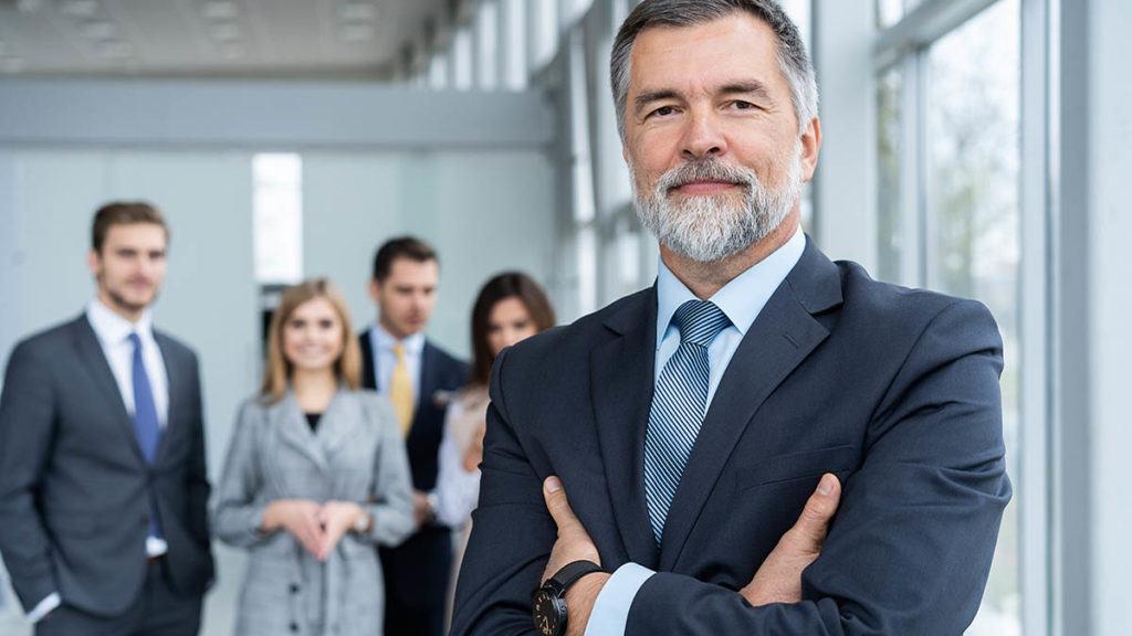 Senior businessman in office standing in front of the team