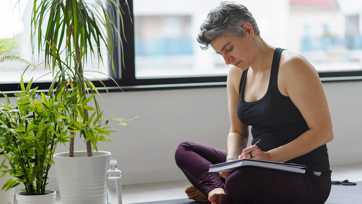 Woman sitting on yoga mat in workout clothes writing in her notebook