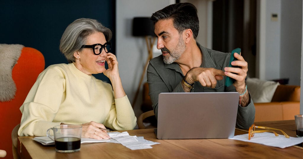 Couple reviewing bills and checking finances on a laptop at the kitchen table, illustrating how to organize your finances and get your financial house in order