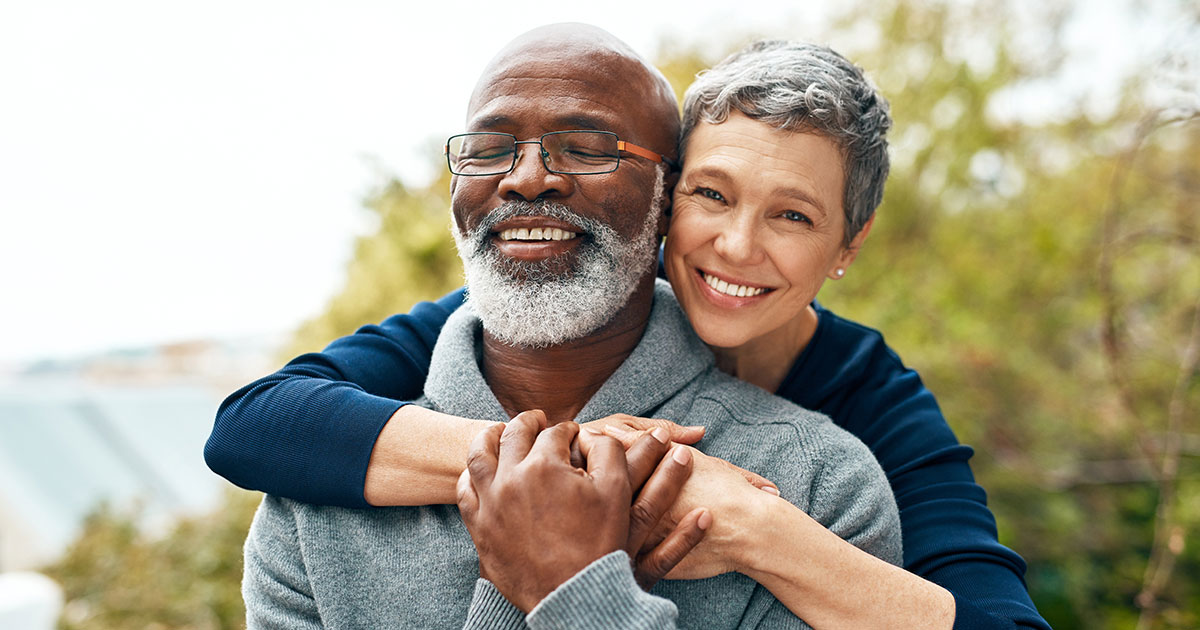 Retired couple embracing outside and smiling.