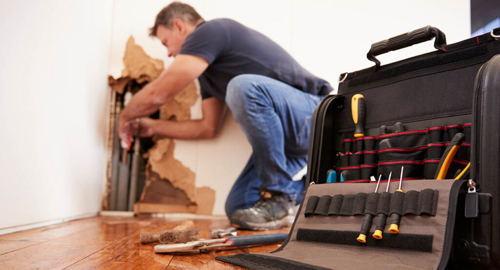 Man repairs a burst pipe in living room wall