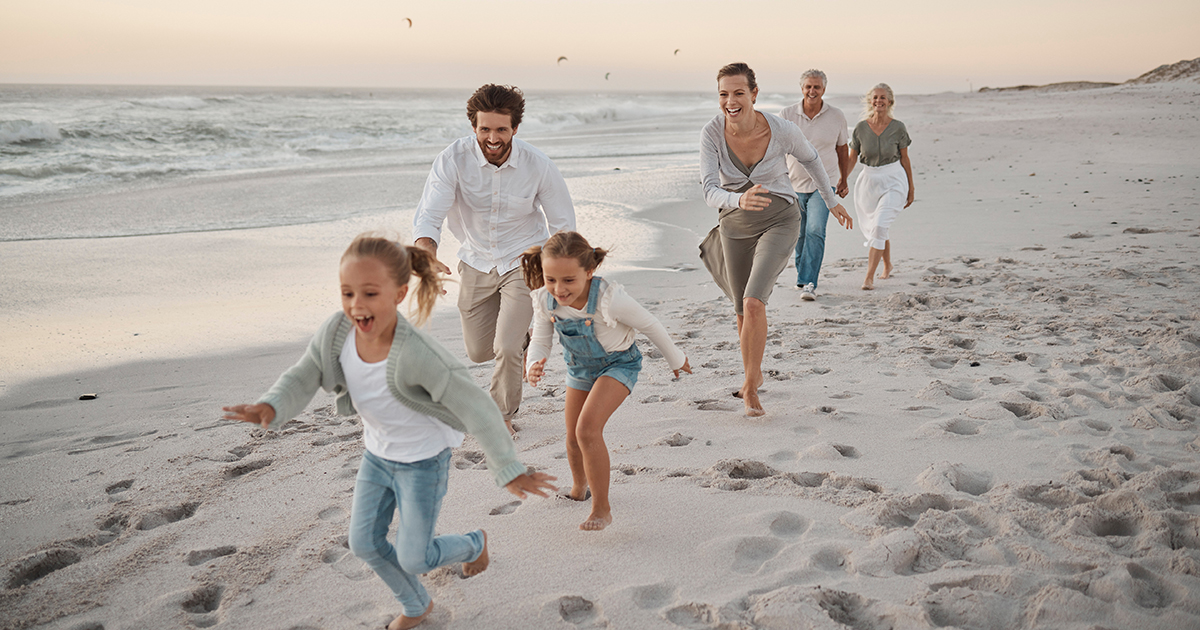 Parents, children and playful with running, beach and excited with grandparents on vacation in summer. Big family, kids and generations at sunset, care and bonding with games by ocean in Spain.