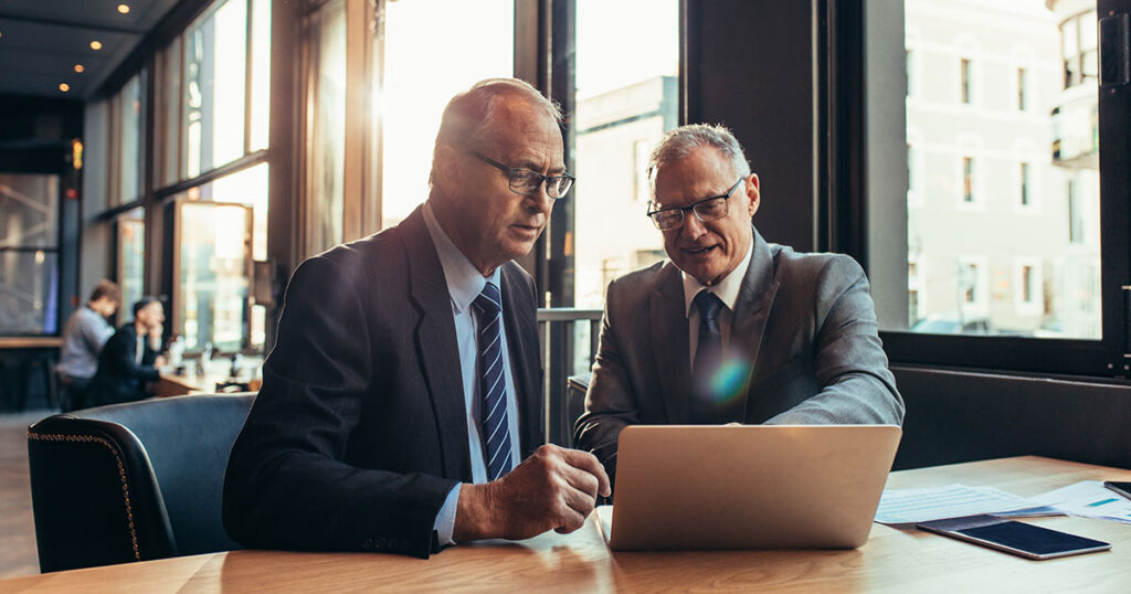 Two financial professionals in suits reviewing information on a laptop in a modern office, discussing private credit investment strategies.