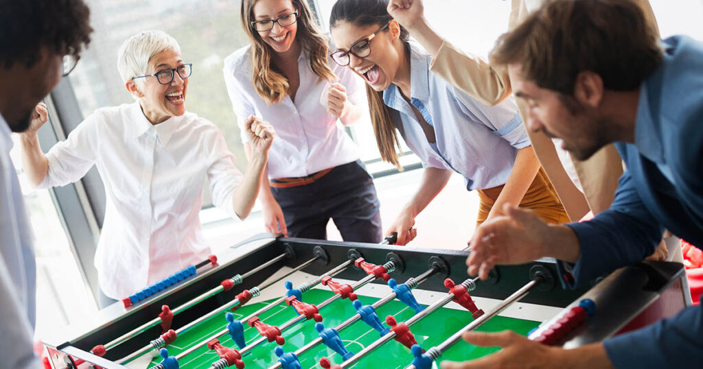 Coworkers of various ages work together playing foosball