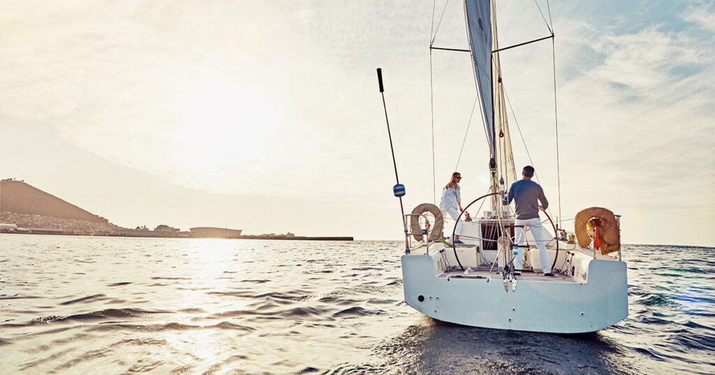 Couple standing on the deck of a sailboat at sunset, symbolizing protection and peace of mind on the water.