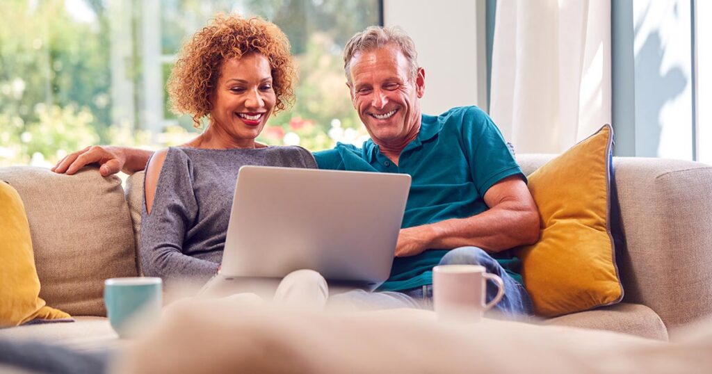 Mature couple smiling while reviewing investment and tax planning strategies on a laptop, representing an enhanced direct indexing approach for high-net-worth portfolios.