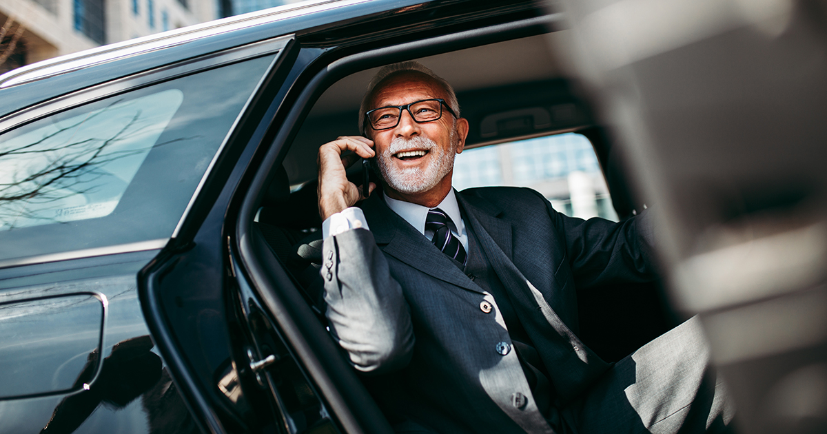 Older man getting out of back of car and on business call