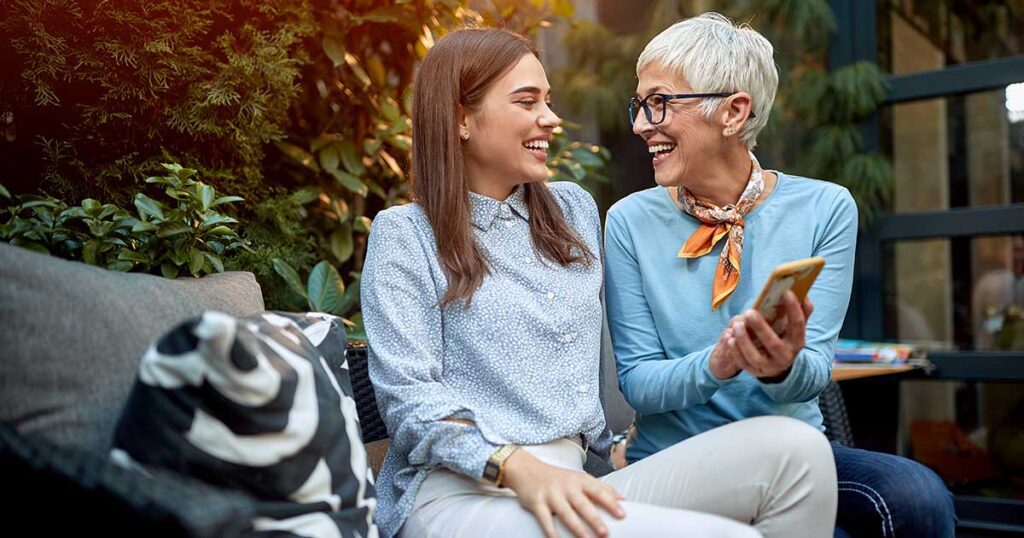 Mother and adult daughter smiling while discussing family legacy and estate planning on a smartphone outdoors