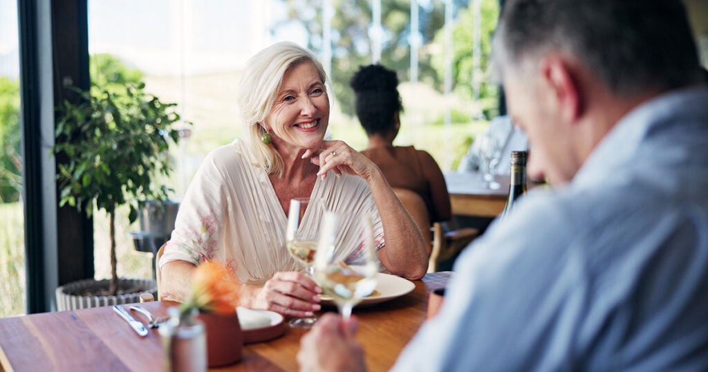 Older couple enjoying a relaxed meal together at a restaurant with glasses of white wine.