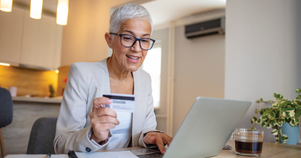 Woman reviewing financial information on a laptop and holding a credit card at her kitchen table
