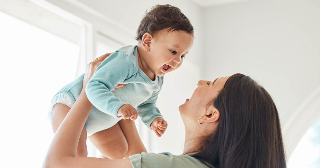 Parent holding up smiling baby at home to symbolize saving and investing for a child’s future.