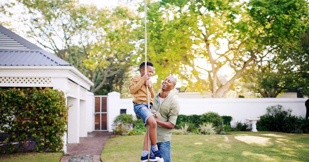 Father helping child swing on a rope in the backyard of a suburban home