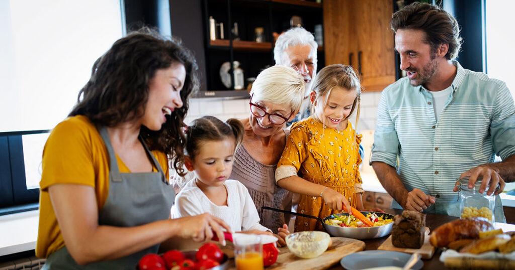 Multigenerational family preparing a meal together in the kitchen, representing coordinated family office risk management strategies to protect and preserve family wealth across generations