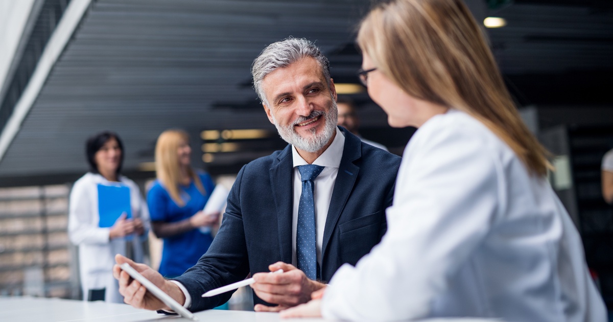 Financial advisor reviewing information on a tablet with a physician in a hospital setting
