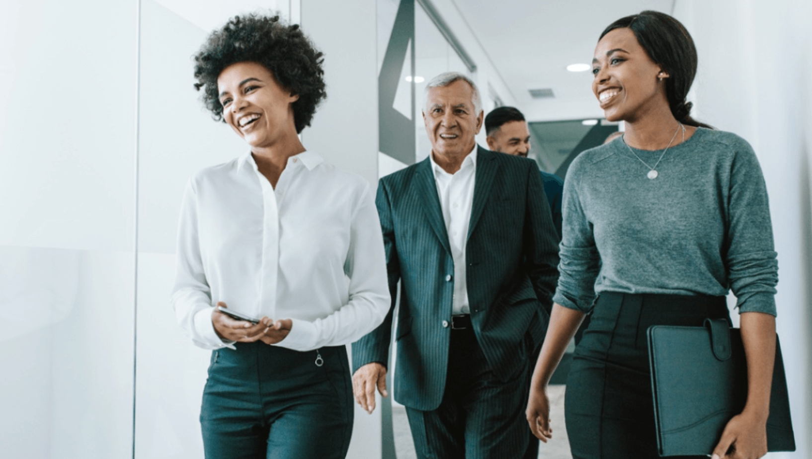 A diverse team of financial professionals walking and smiling in a modern office, representing the coordinated planning needed for business owner succession and retirement.