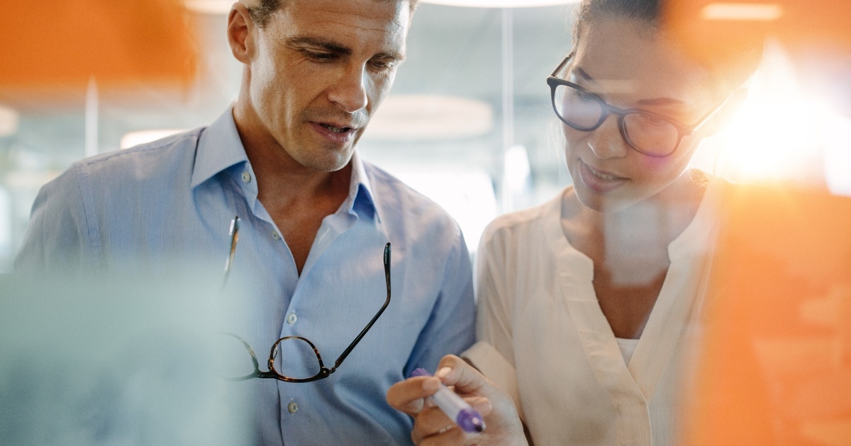Two tech coworkers collaborating in front of a glass board, representing coordinated ESPP strategy and stock purchase planning within an overall financial plan