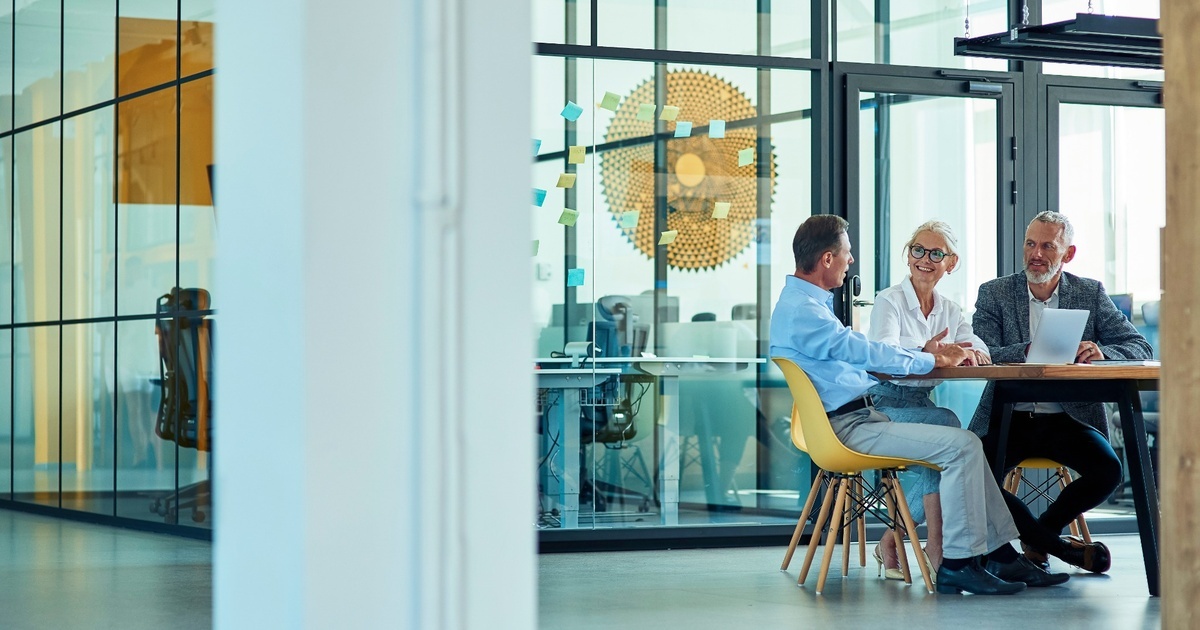 Three professionals meeting in a modern glass-walled office, representing tech executives working with advisors to manage concentrated company stock risk