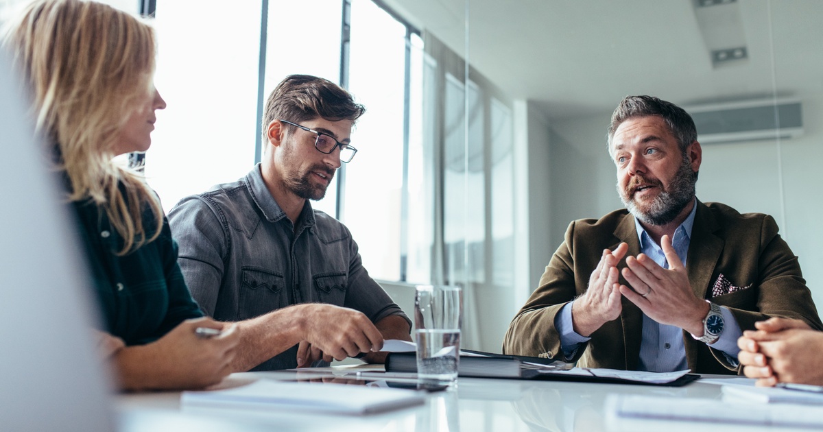 Group of professionals meeting around a conference table in a glass-walled office, representing advisors evaluating private market and alternative investment options within a wealth plan