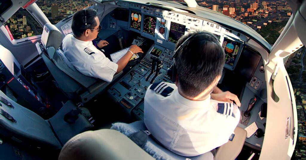 Two pilots in an airline cockpit during flight, with a city visible below