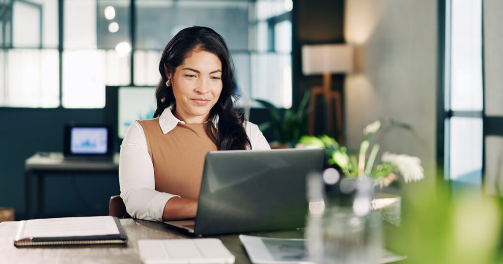 A business professional reviewing financial records and documentation on a laptop in an office setting.