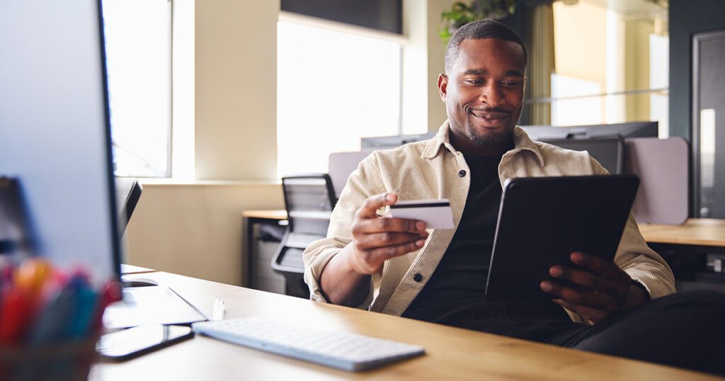 A person holding a credit card while looking at a tablet, representing credit card fraud prevention.