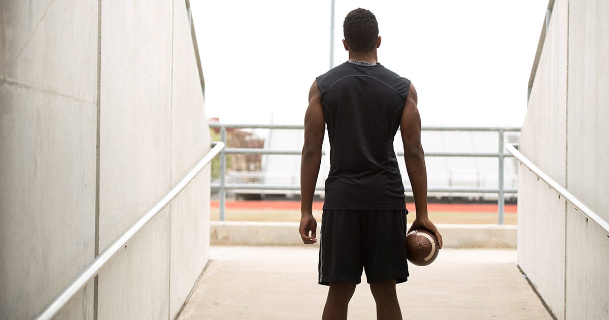 College football player holding a football and walking out of the tunnel toward the stadium field