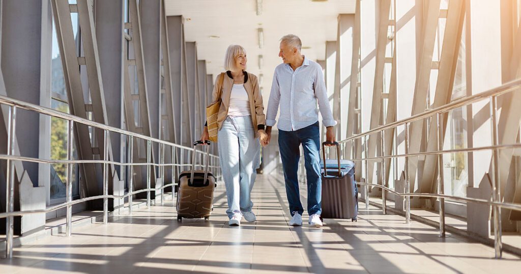A retired couple walking together with luggage through an airport terminal or walkway, representing confident retirement travel planning.