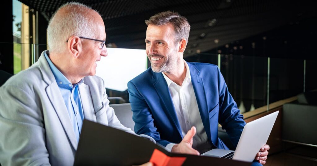 An older business owner reviews a folder with a Creative Planning business exit planning advisor who holds a laptop in a modern office.
