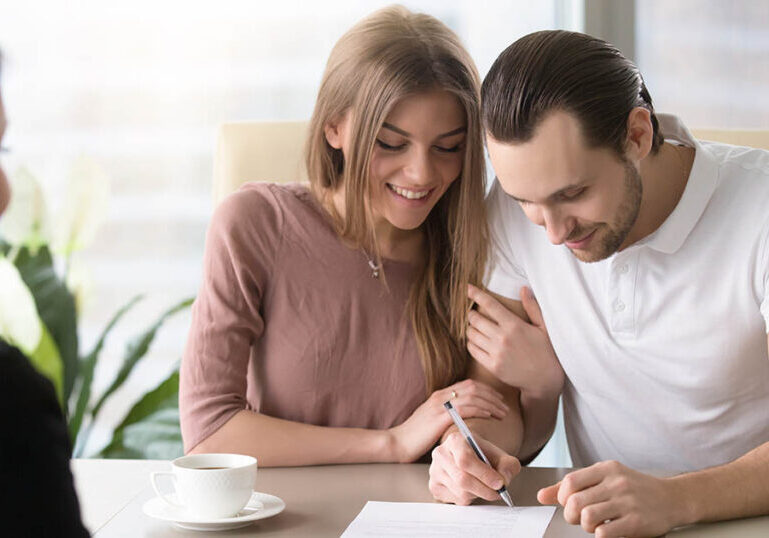 Smiling couple agreed to sign prenuptial contract, handsome man putting signature on document while sitting together with his wife, taking bank loan, health insurance, signing financial papers