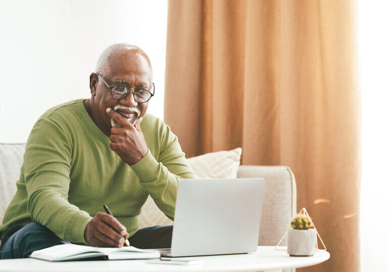 Senior man reviewing financial documents on a laptop while organizing his estate planning affairs.